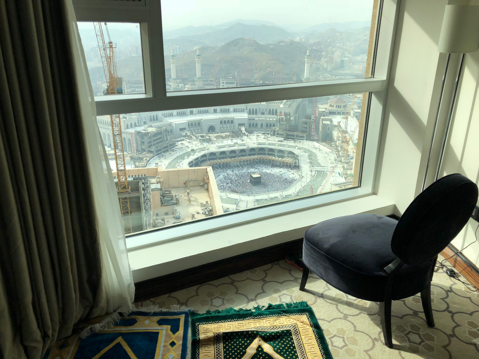 View of the Kaaba and Masjid al-Haram from a hotel room window with prayer mats laid out